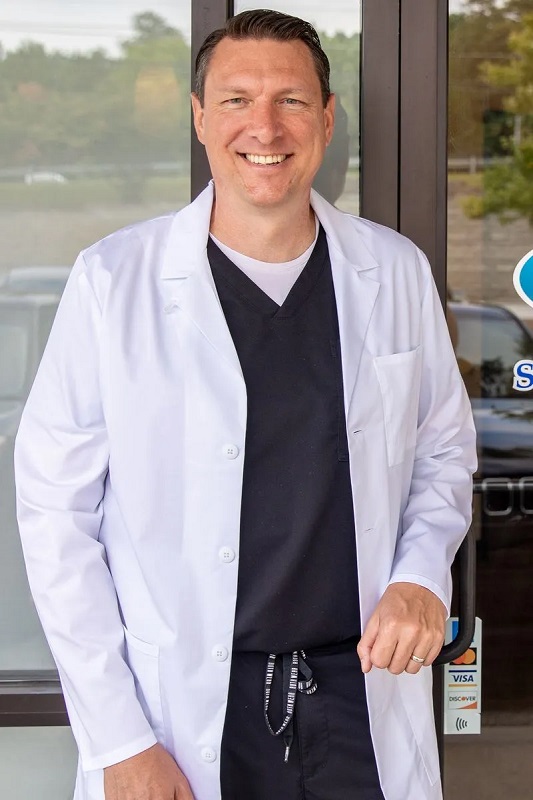 Dr. Stephen Wilson, DMD standing at the entrance of Stress Free Dentistry wearing a white lab coat over black scrubs.