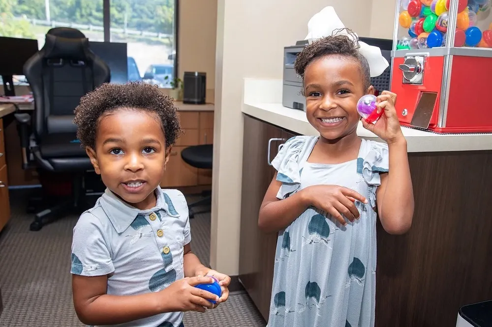 Two young children smiling and holding toy capsules next to the prize vending machine at Stress Free Dentistry.