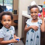 Two young children smiling and holding toy capsules next to the prize vending machine at Stress Free Dentistry.