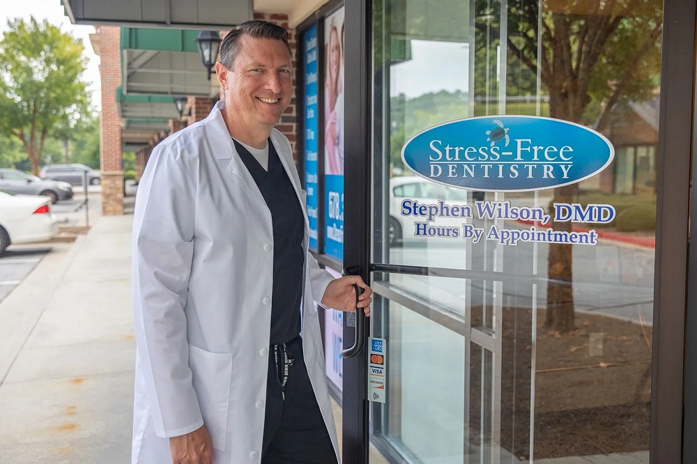 Dr. Stephen Wilson, DMD in a white lab coat opening the front glass door of Stress Free Dentistry clinic.