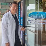 Dr. Stephen Wilson, DMD in a white lab coat opening the front glass door of Stress Free Dentistry clinic.