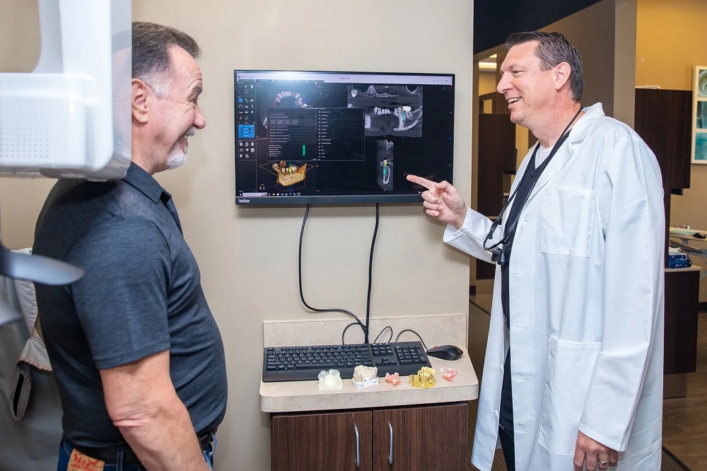 Dr. Stephen Wilson reviewing 3D digital imaging scans on a wall monitor with a male patient.