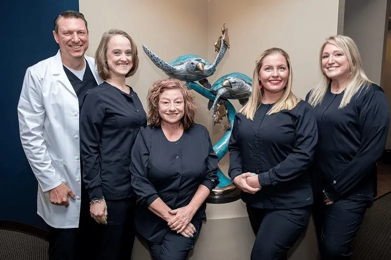 Dr. Stephen Wilson and dental staff in black scrubs smiling near sea turtle decor at Stress Free Dentistry.